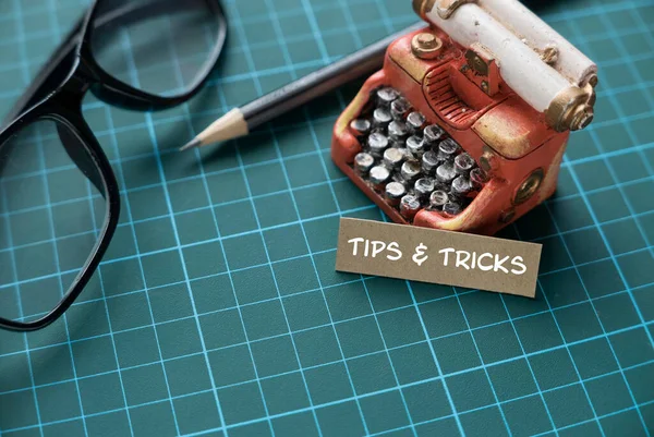 Tips and tricks concept with miniature typewriter, pen and glasses on a green craft mat.