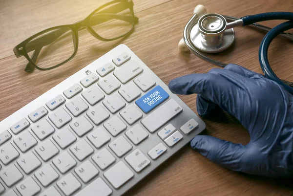 A hand wearing a blue glove pointing a finger to a blue computer keyboard written with Ask Your Doctor.