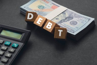 Wooden cube written with DEBT , calculator and money on a black background.