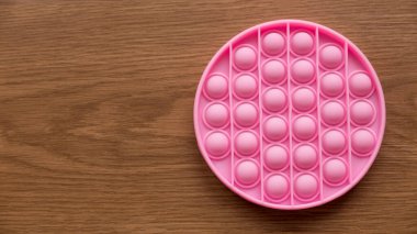 Top view of a pink anti stress sensory toy fidget push pop it on a wooden background with copy space.