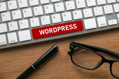 Pen. glasses and computer keyboard with a red button written with Wordpress.