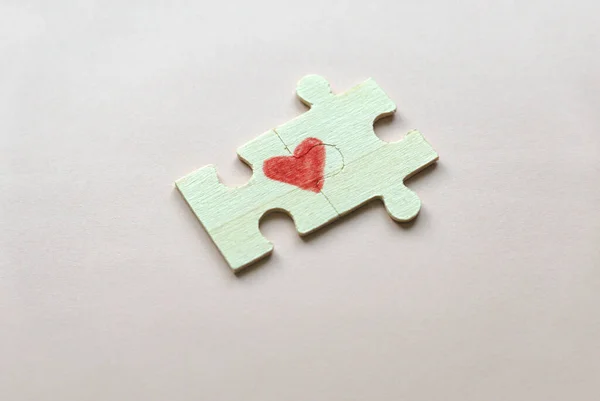 Selective focus of two pieces of a puzzle forming a heart on a pink background. Love concept.