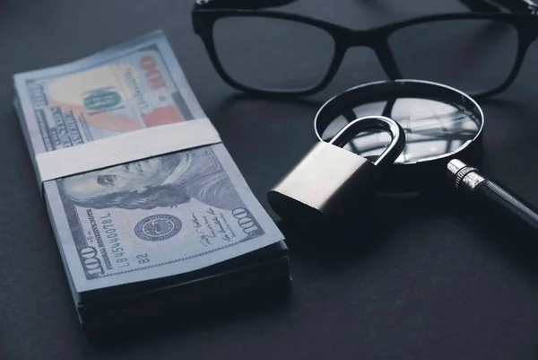 A money, magnifying glass, glasses and padlock on a black background.