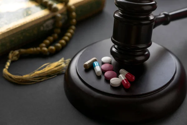 Concept of sharia law and drugs. Medicine pill and tablet, with gavel, holy Quran and rosary beads on a black background.