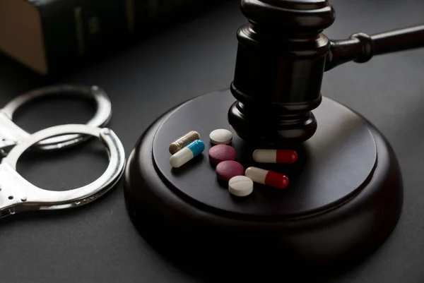 Drugs and law concept. A medicine pills and tablets with handcuff and gavel on a black background.