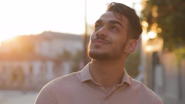 Közelkép férfi boldog ihletett szakállas arc. Portré arab spanyol üzletember fiatal felnőtt töprengő fickó áll a városban az utcán hátterében naplemente nap álmodik gondolkodás élvezi sugarak nyáron — Stock videók