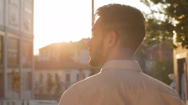 ［戻る］ビューのヒスパニックアラビア語成功した若い大人のビジネスマンのリーダーのボス男のマネージャーの労働者は、夕日の街の建物の古い都市の背景に立つ太陽の黄金の空を屋外で歩いて楽しむ — ストック動画