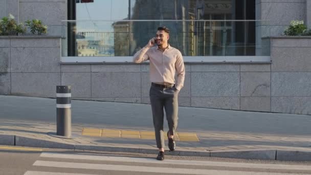 Hispánský arabský mladý dospělý podnikatel kráčející s mobilním telefonem na ulici pěší křižovatce silniční dopravy. Šéf byznysmen volat smartphone venku. Veselý chlap venku mluví o mobilu — Stock video