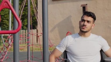 Tekerlekli sandalyede sakat bacakları olan genç bir adam ellerini stadyumda kullanıyor. Sürekli özgüvenli engelli kişi Engelli Olimpiyatları için hazırlanıyor. Yaralı sporcu simülatörde egzersiz yapıyor