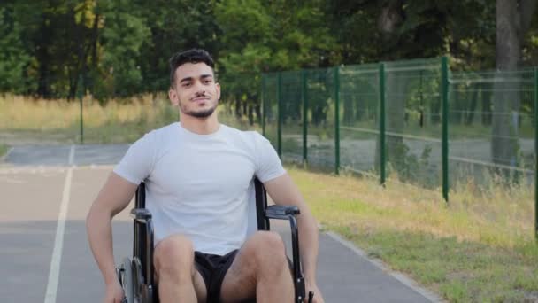 Ung Mellanösternarabisk man med funktionshinder rider rullstol på sommarstadion löpband, handikappade person förbereder sig för paralympiska spel. Millennial kille idrottsman led idrottsskada i träning — Stockvideo