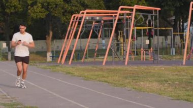Amatör sporcu Hintli sporcu, spor giyim ve spor ayakkabılarında koşuyor. Koşu bandında koşuyor. Saati kronometreyle kontrol ediyor. Orta Doğulu sporcu spor sonuçlarını izlemek için akıllı telefon özelliklerini kullanıyor