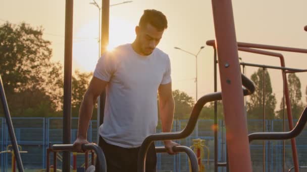 Сильный арабский человек выполняет отжимания на решетках развивается бицепсы и трапециевидные мышцы, делая машинные упражнения во время ежедневной тренировки. Молодой энергичный спортсмен с Ближнего Востока тренируется на стадионе — стоковое видео