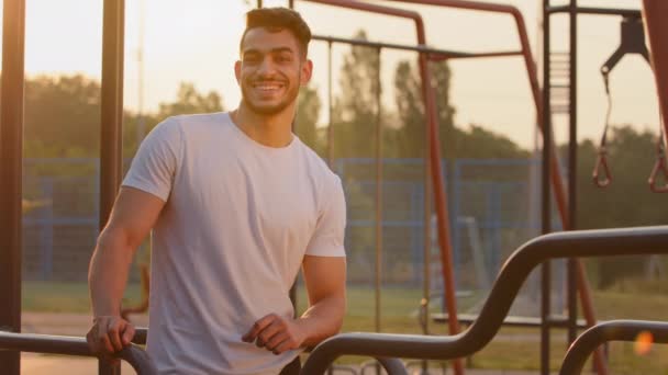 Millennial μυϊκή Ισχυρός Άραβας με καλό μυϊκό ιστό, αντλείται μέχρι τους μυς χαλάρωση μεταξύ των ασκήσεων κατά τη διάρκεια της πρωινής άσκησης. Νεαρός ελκυστικός χαμογελαστός Ινδός αθλητικός τύπος της Μέσης Ανατολής — Αρχείο Βίντεο