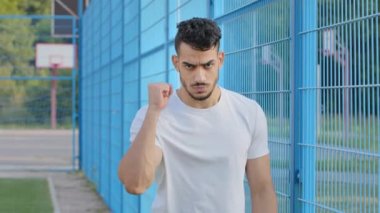Kızgın futbol fanatiği genç Arap İspanyol erkek atlet sıkılmış yumruğuyla el sallıyor, Orta Doğu Hindistanlı adam rakiplerini tehdit ediyor, agresif davranış, güç ve saldırganlık gösteriyor