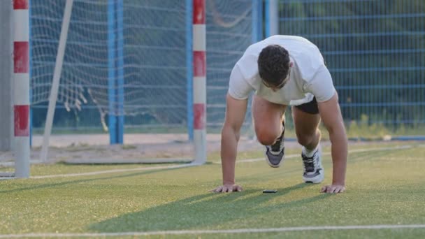 El futbolista de Oriente Medio entrena piernas, se mantiene en forma durante el entrenamiento diario del estadio, se prepara para el partido o el campeonato. Millennial atleta de fútbol chico indio en ropa deportiva de verano haciendo ejercicio de levantamiento de piernas — Vídeos de Stock