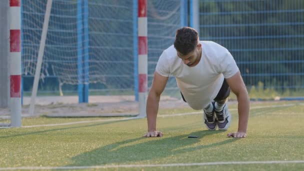 Junge Sportler Fußballer indischer Typ in Sommersportbekleidung, der Bizeps-Liegestützübungen macht und während des Trainings die Arme trainiert. Nahost-Athlet trainiert morgens vor dem Spiel im Stadion — Stockvideo