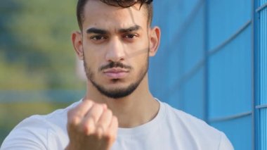 Yakın plan kızgın, huysuz, genç, Arap, Latin asıllı sporcu öğrenci kameraya yumruk sallıyor, saldırganlık gösteriyor, savunuyor. Orta Doğulu Hintli adam el hareketi yapıyor.