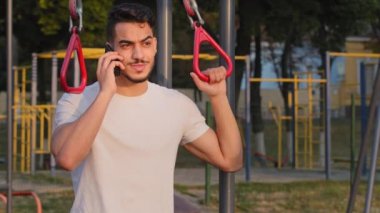 Spor kıyafetli Hintli adam spor salonunda spor salonunda spor yaparken telefonla konuşuyor. Orta Doğu Arap milenyum atleti stadyumda dikilip akıllı telefon konuşuyor.