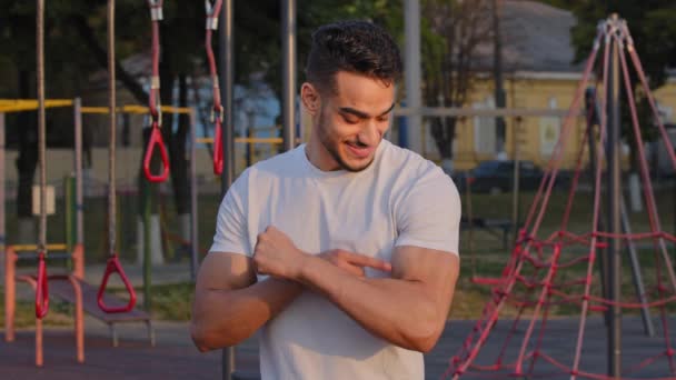 Bombeado deportivo milenario Oriente Medio árabe chico muestra grandes bíceps, orgulloso de los logros atléticos. Joven deportista indio presenta hermosos músculos corporales en el entrenamiento matutino al aire libre en el campo de deportes — Vídeo de stock