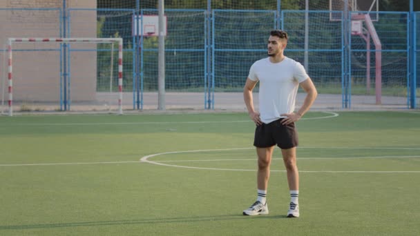 Fiatal tapasztalt edző indiai srác nyáron sportruházat áll a focipályán az iskola stadion felkészül a képzés, várja a sportolók futballisták. Közel-keleti sportoló szünetet tart — Stock videók