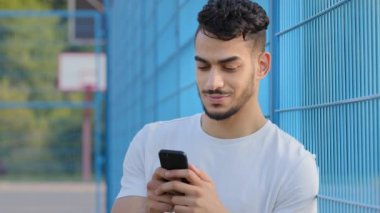 Yazın spor giyim kuşağında genç bir Arap atleti cep telefonu kullanıyor, sanal uygulama kullanıyor, akıllı telefonda online servis yapıyor, mesaj yazıyor, daktilo ediyor, ekrana dokunuyor, stadyumda duruyor.