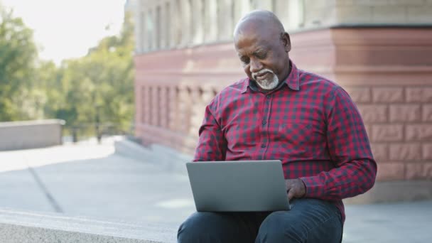 60歳のアフリカ系アメリカ人高齢者のお客様は、ラップトップ屋外ショッピングをオンラインで。高齢銀行のクライアントの男性は、インターネットストアで良い買って、サービスショーに満足しますokジェスチャーをお勧めしますアプリ — ストック動画