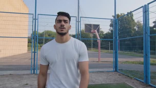 疲惫的年轻的中东阿拉伯运动员在夏天穿着运动服沿着体育场篱笆行走，擦去额头上的汗珠，经过长时间艰苦的锻炼、跑步或踢足球后呼吸急促 — 图库视频影像