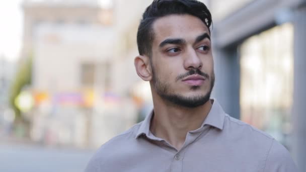 Zamknij portret młodego brodatego arabskiego człowieka stojącego na ulicy miasta i rozglądającego się uważnie pijącego herbatę z papierowej filiżanki. Latynoski biznesmen myśli, że odpoczywa pije kawę i patrzy na budowę — Wideo stockowe
