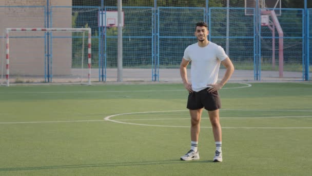 Aantrekkelijke atleet, Indiase man in de zomer sportkleding rusten tussen trainingsoefeningen ademen frisse lucht. Midden-Oosterse sportman neemt pauze, glimlachend vrolijk staand op stadion voetbalveld — Stockvideo