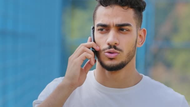 Серьёзно обеспокоенный молодой ближневосточный студент-арабский спортсмен летом в спортивной одежде держит смартфон, индиец разговаривает по современному мобильному телефону, сообщая плохие новости, ведет неприятный разговор — стоковое видео