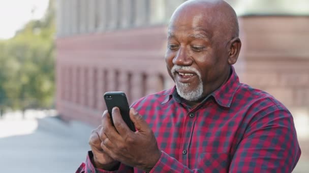 Feliz contento anciano negro abuelo hombre haciendo videollamada, mirando la cámara del teléfono inteligente, mostrando el pulgar hacia arriba gesto de aprobación, Africano americano maduro decir buenas noticias hablando en el teléfono móvil moderno — Vídeo de stock