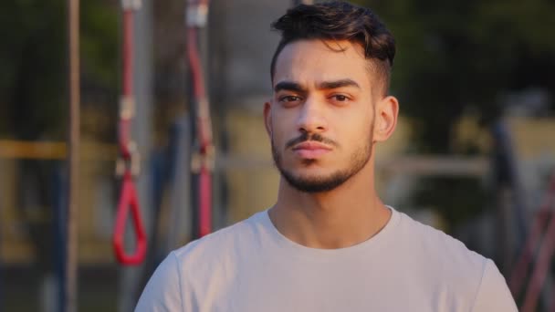 Πορτρέτο του Millennial ελκυστική Άραβας φοιτητής άνθρωπος με ευρύ λευκό φιλικό χαμόγελο. Νέοι Μέση Ανατολή ινδική mustachied αθλητικός τύπος στο αθλητικό ντύσιμο κοιτάζοντας κάμερα ποζάρουν στο γήπεδο της πόλης το καλοκαίρι — Αρχείο Βίντεο
