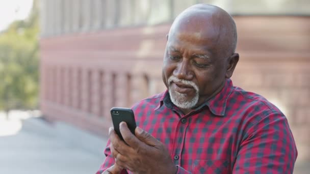 Tipo tranquilo abuelo negro senior hace videollamada, mira a la cámara del teléfono inteligente, afroamericano hombre maduro anciano se comunica con los nietos utilizando el teléfono móvil moderno comparte buenas noticias — Vídeos de Stock