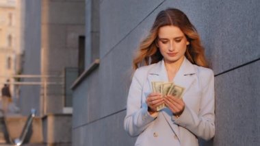 Başarılı zengin beyaz iş kadını sokak şehrinde duruyor, paraları sayıyor, banknotları sayıyor, bütçe hesapları, rüşvetler, finansal ödemeleri düşünüyor, servetleri düşünüyor.