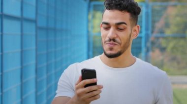 Mutlu Ortadoğu Arap atleti yazın spor giyim kuşağında sanal uygulama kullanarak video görüşmesi yapıyor, akıllı telefondan online servis yapıyor, Hintli adam kameraya bakıyor, modern cep telefonuyla konuşuyor. 