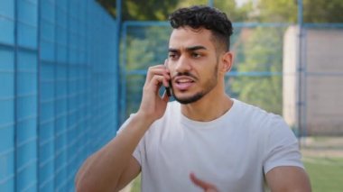 Kızgın, agresif, sinirli, genç, Ortadoğu Arap atleti spor kıyafetleri içinde elinde akıllı telefon, endişeli, öfkeli, öfkeli Hintli bir adamın cep telefonunda bağırması hoş olmayan bir konuşma.