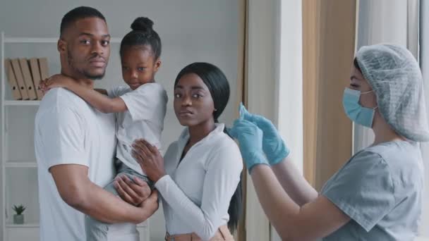 Ciddi Afrikalı aileler, genç siyah afro ebeveynler ve küçük kızı Kafkasyalı kadın doktor hemşirenin yanında hastane laboratuvarında şırıngayla, aşılama aşısıyla duruyorlar. — Stok video
