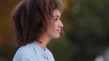 Pozitif iş kadını genç Afro-Amerikalı kız model müşterimiz uzaktan bakar ve dişçi servisinden memnun bir şekilde şehirde oturmuş gülümseyen dişleğe bakar.