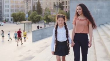 İspanyol aile annesi ve küçük kız öğrenci kız dışarıda yürüyüp sohbet ediyorlar. Küçük çocuk annesiyle okula gidiyor. Okul derslerine gidiyor. İletişim kuruyor.