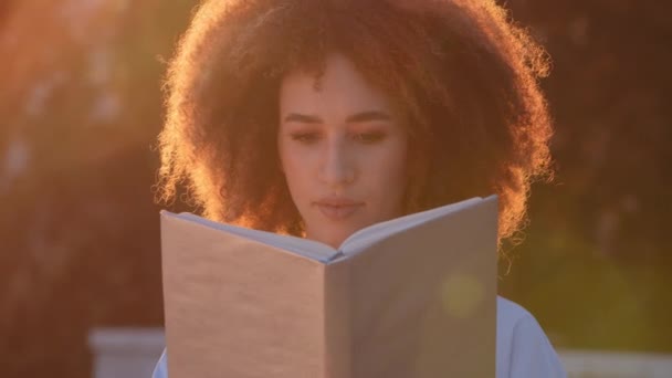 Portret van krullend Afrikaans Amerikaans meisje student afro gemengd ras vrouw vrouwelijke studie lezen boek schoolboek toont shakes index vinger eens met lezen informatie leert zitten buiten in het zonlicht — Stockvideo