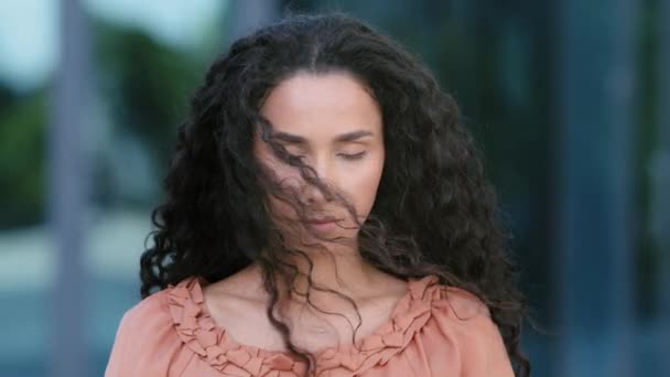 Kvindelige portræt udendørs brunette hispanic etnisk blandet race kvinde alvorlig ked frustreret dame model ser op ser på kameraet retter hår streng stående i byen i blæsende vejr – Stock-video