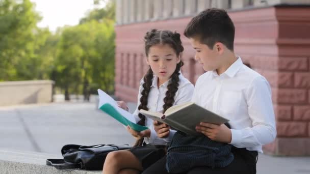 Çocuklar, iki okul çocuğu İspanyol küçük kız öğrenci ve erkek öğrenci açık havada kitap okuyorlar çocuk günlük tutuyor kötü davranışlar için notlar atıyor dikkat dağıtıcı defterleri atıyor kollar çapraz — Stok video