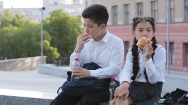 İki çocuk okul tatilinde dışarıda çörek yiyor, aç öğrenciler öğle yemeği yiyor, erkek kardeş ve kız kardeş İspanyol çocuklar hamur işi yiyor, yemek yiyor şişeden temiz su içiyor.