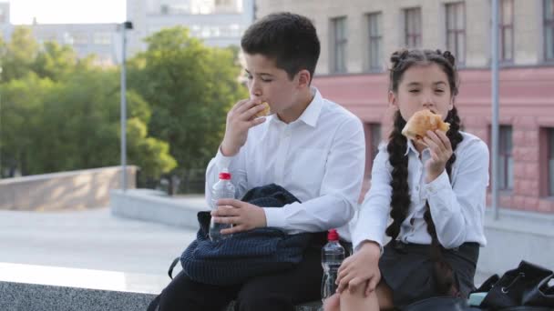 İki çocuk okul tatilinde dışarıda çörek yiyor, aç öğrenciler öğle yemeği yiyor, erkek kardeş ve kız kardeş İspanyol çocuklar hamur işi yiyor, yemek yiyor şişeden temiz su içiyor. — Stok video