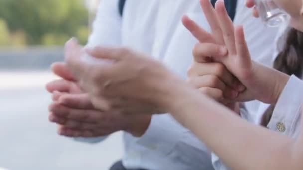 Donna irriconoscibile madre insegnante e scolari compagni di classe ragazza e ragazzo trattamento palme da batteri spruzzando con alcool rimedio anti-virus, primo piano sfregamento mani pulizia lavaggio da covid — Video Stock