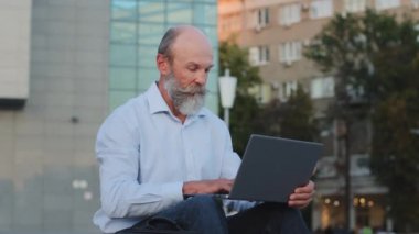Dışarıda dizüstü bilgisayar kullanan yaşlı aktif emekliler internetten çalışıyorlar. Gri sakallı yaşlı kişi modern teknoloji, bilgisayar uygulaması ve e-posta kullanıyor, sosyal ağlar üzerinden iletişim kuruyor