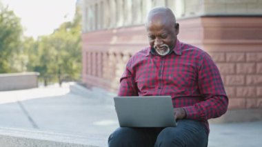 Tatmin olmuş Afro-Amerikan müşterisi yaşlı bir adamın, hizmetlerinden memnun olmayan bir jest göstermesi, web sitesini tavsiye ediyor. Uzaktan kumandayla çalışıp, online bahis oynayarak, haber almaktan mutlu, yüksek kârlı.