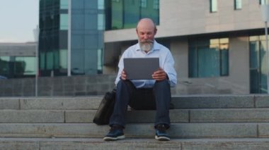 Dizüstü bilgisayarın el sallamasına bakan gri sakallı yaşlı Avrupalı bir adam akrabalarıyla hoş sohbetler yapıyor. Yaşlı büyükbaba internetten iletişim kurmak için modern teknolojiyi kullanıyor.