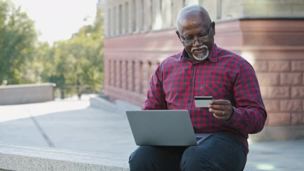 Senyum pelanggan bank dewasa. Afrika Amerika pria duduk dengan laptop menggunakan layanan aplikasi e-banking. Pemegang kartu kredit puas dengan prosedur pembayaran keamanan yang mudah menerima manfaat sebagai klien setia — Stok Video