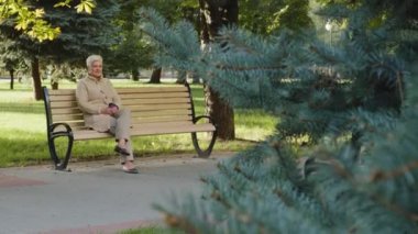 Serin havalarda güneşli bir günde, rahat, gri saçlı, yaşlı bir büyükanne, günlük sıcak giysiler içinde bankta oturuyor. Emeklilik yaşında çekici olgun bir kadın açık havada vakit geçiriyor.
